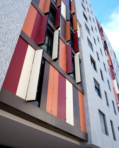 Fachada Edificio Torres Las Palmas, revestimiento en gris y marrón, persianas naranjas, rojas, marrones y crema.